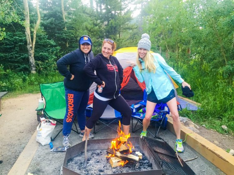 three women pose proudly in front of a campfire