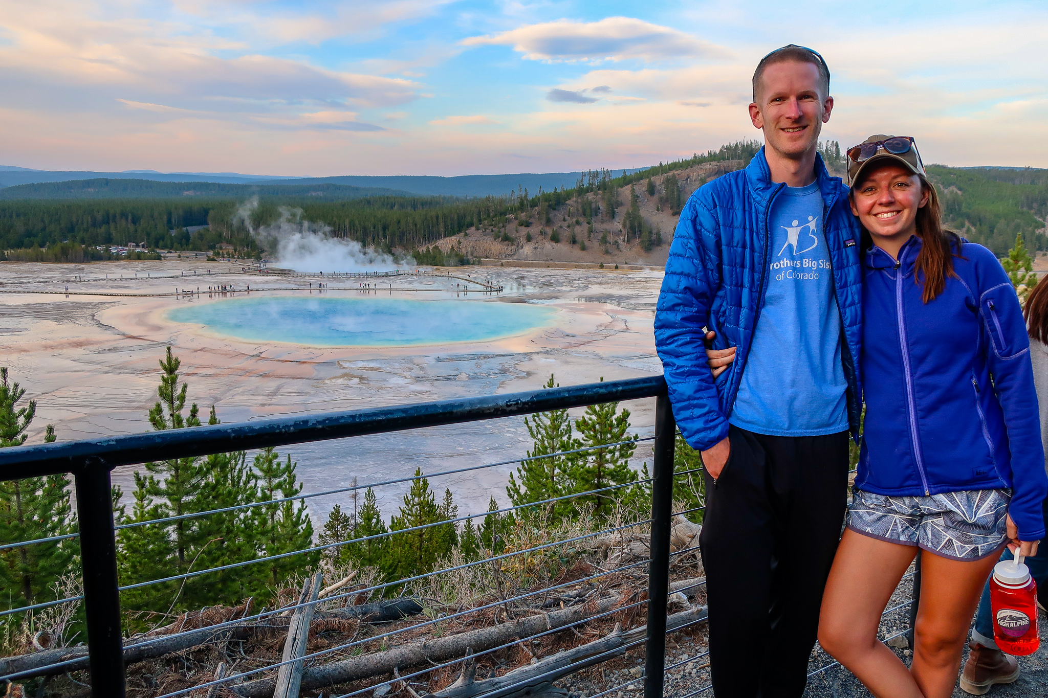 couple stands at the grand prismatic hot spring overlook in yellowstone national park at sunset