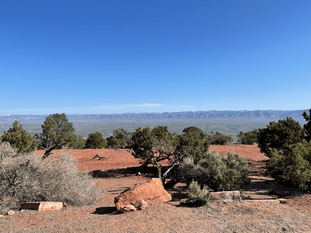 desert mesa in the foreground; beyond the edge of the mesa is a panoramic view of the Grand Valley in western Colorado